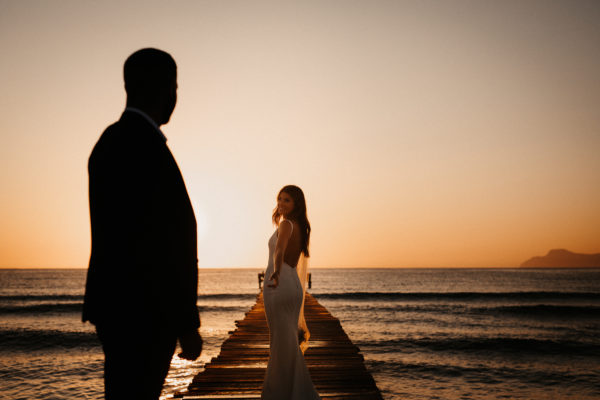 Die Braut reicht ihrem Mann die Hand auf einem Holzsteg am Strand auf Mallorca
